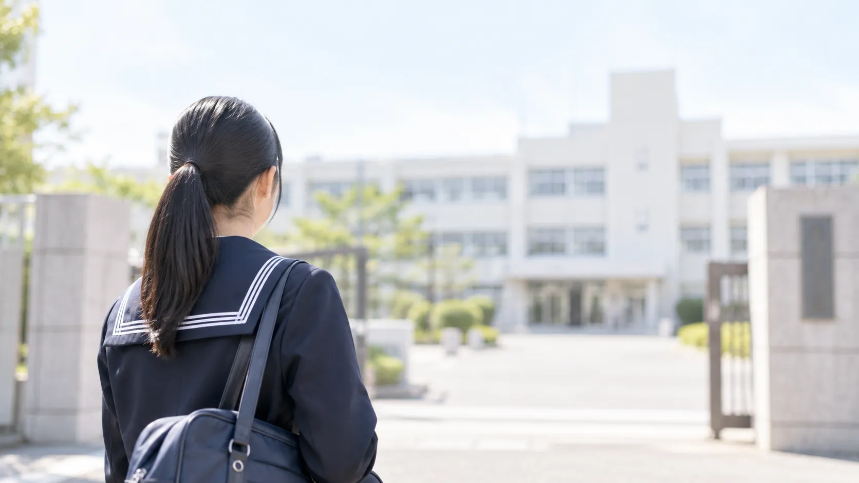高校の正門の前で校舎を見つめる中学生の後ろ姿
